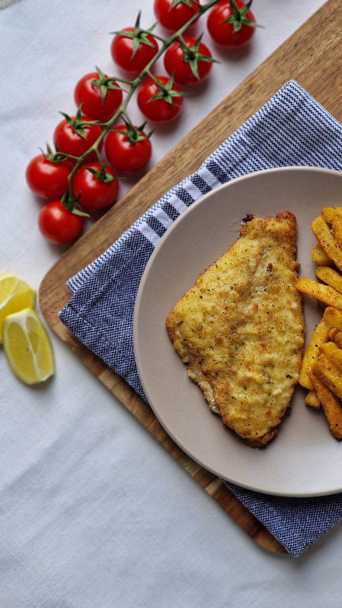 Delicious crispy fish with seasoned chips and fresh cherry tomatoes on a wooden board.